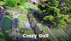 A large section of a crazy golf course surrounded by trees, with a partial view of the hills of Cheddar